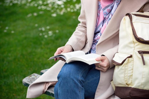 The girl is sitting on a park bench and reading a book