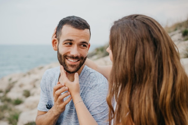 A girl is stroking with her hands the face of her boyfriend on the rocky hill