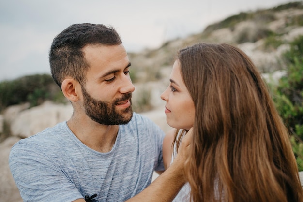 A girl is stroking with her hands the face of her boyfriend on the rocky hill