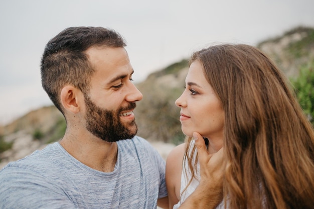 A girl is stroking with her hands the face of her boyfriend on the rocky hill