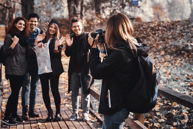 Girl is taking a photo of her friends in the autumn golden park.