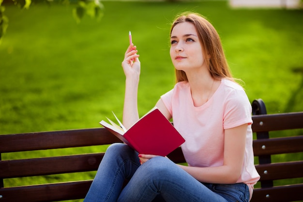 Girl is thinking what to write in a notebook, sitting in the Park