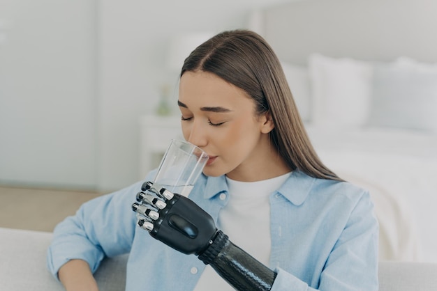 Girl is using futuristic arm prosthesis holding glass of water Healthy lifestyle after amputation