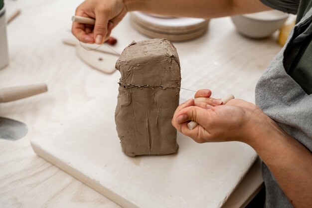 Photo girl is using a wire cutter to cut off a piece of clay before modeling the product slicing off a chunk of clay from a large block using a sharp wire clay cutter