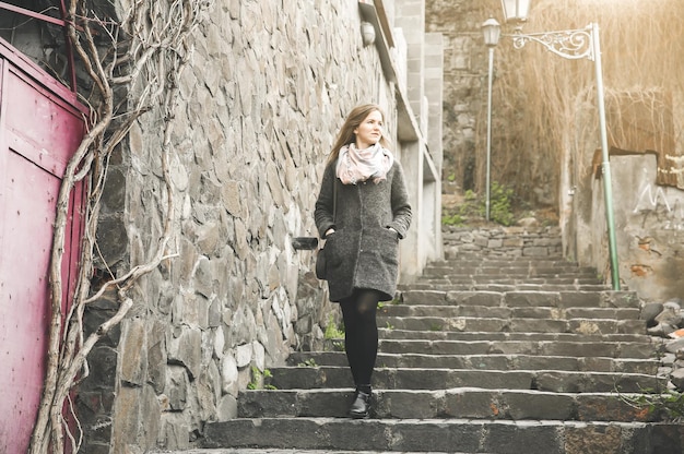 Girl is walking in the narrow street with stone pavement Stylish woman Medieval lantern Stairs in the city