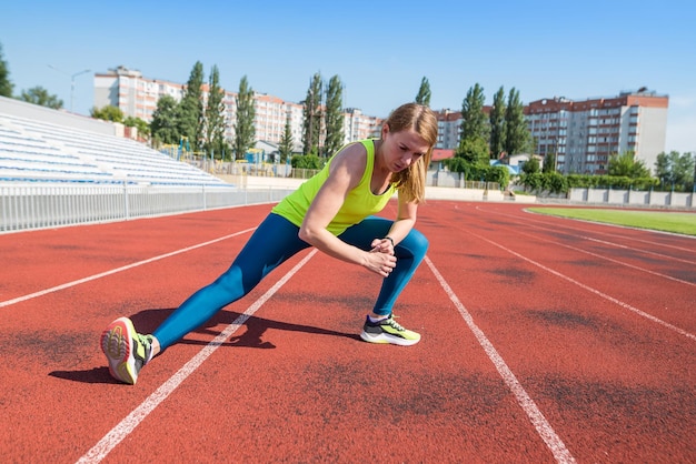 The girl is warming up at the stadium Sportswoman stretches leg muscles before jogging Training at the city sports stadium