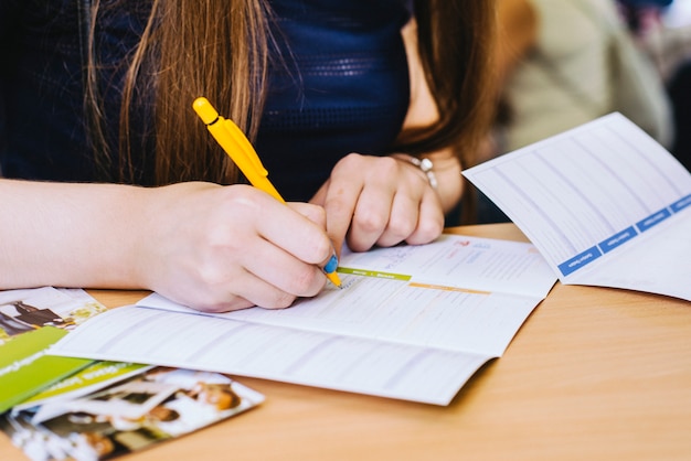 Girl is writing form with yellow pen in blue shirt on the wooden table