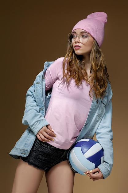 Girl in jeans a pink hat and stylish glasses with a ball