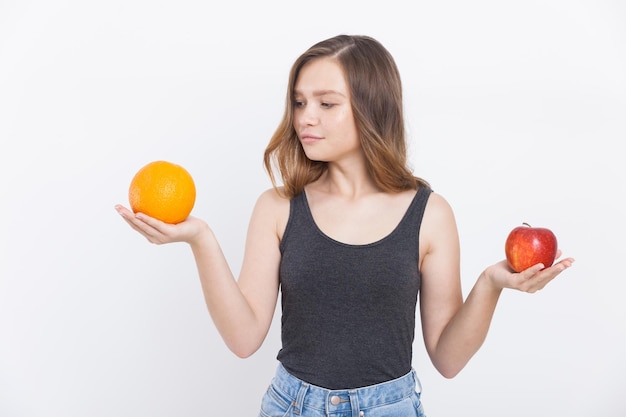 Girl in jeans and tank top holding apple and orange