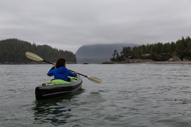 Girl kayaking in the ocean during a cloudy and gloomy sunrise