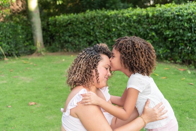 A girl kisses her mother on the forehead in the open air