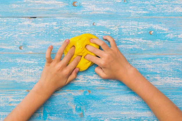 Girl kneads a ball of yellow slayma on blue wooden table.