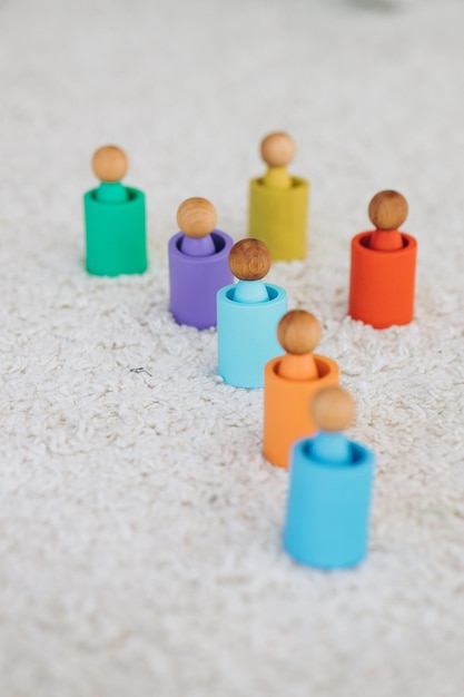 The girl learns colors by playing with wooden cylindrical toy colored human figures and placing them in cups of the appropriate color The child is happy that he completed the task correctly