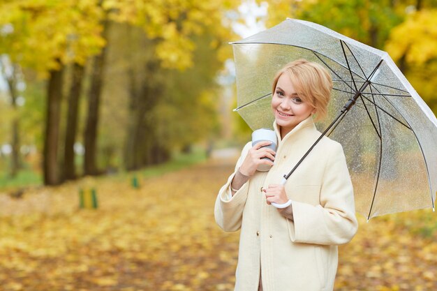 Girl in a light coat with a transparent umbrella in autumn in the park autumn sale concept