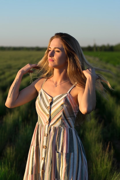 A girl in a light dress in a green field at sunset