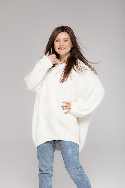 Girl in light jeans and a white oversized sweater on a gray background