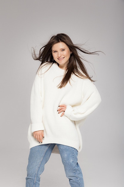 Girl in light jeans and a white oversized sweater on a gray background