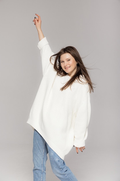 Girl in light jeans and a white oversized sweater on a gray background