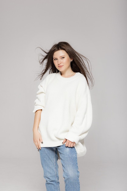 Girl in light jeans and a white oversized sweater on a gray background