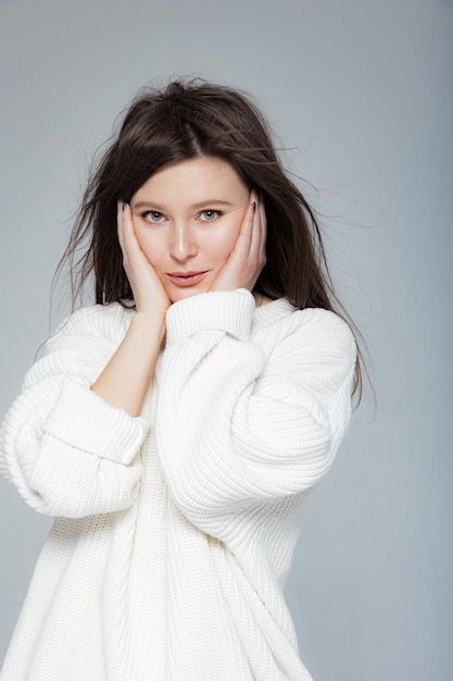 Girl in light jeans and a white oversized sweater on a gray background