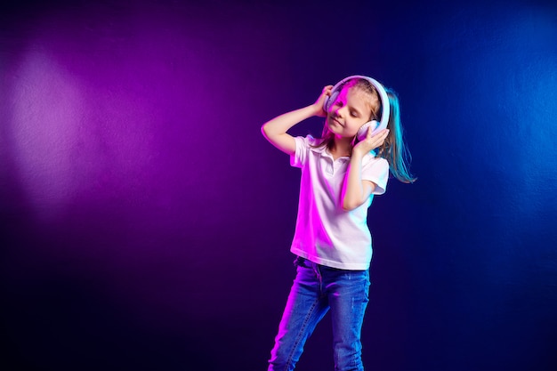 Girl listening to music in headphones on dark colorful . Cute child enjoying happy dance music, close eye's and smile posing   