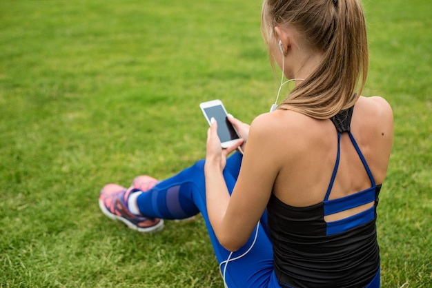 girl listening to music on the phone resting after the marathon sitting on the grass in the stadium 