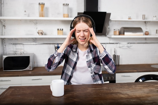 The girl listens to music on headphones and drinks coffee. A woman has a headache