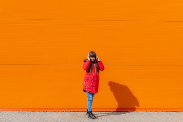 A girl listens to music with headphones on the background of an orange wall Copy space Mockup An article about modern youth An article about modern music Article about the choice of headphones