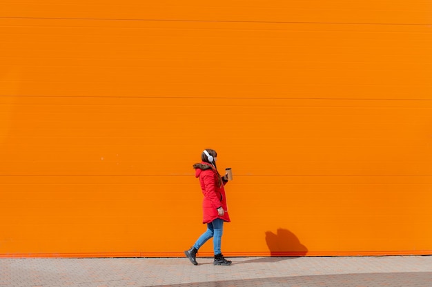 A girl listens to music with headphones on the background of an orange wall Copy space Mockup An article about modern youth An article about modern music Article about the choice of headphones