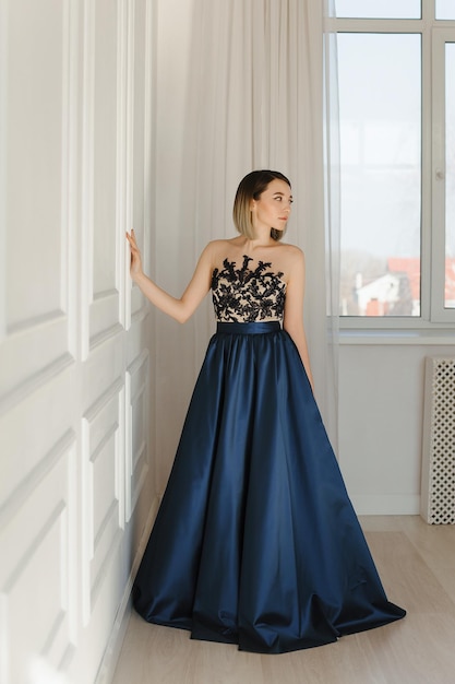 Girl in a long blue evening dress against a white wall