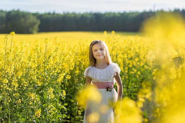 girl in a long white dress in a rapeseed field in summer