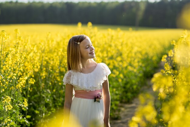 girl in a long white dress in a rapeseed field in summer