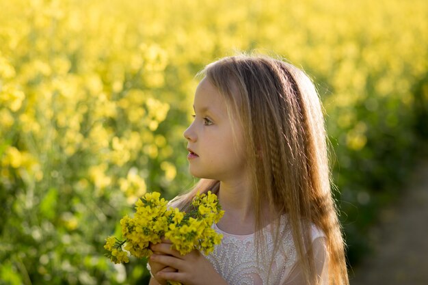 girl in a long white dress in a rapeseed field in summer