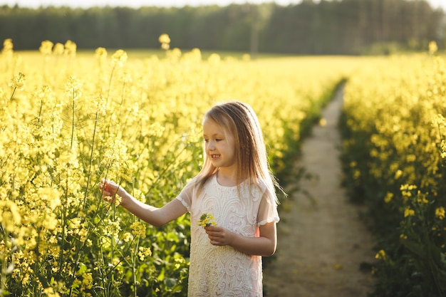 girl in a long white dress in a rapeseed field in summer