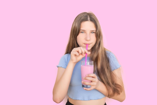 Girl looking at camera and drinking strawberry milkshake with a strawberry pipe on pink background