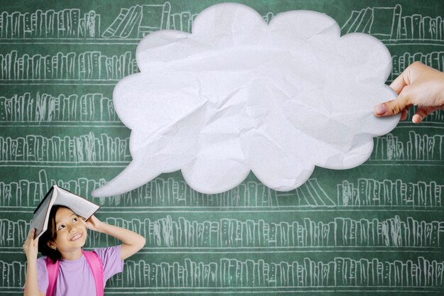 Photo girl looking at cropped hand holding speech bubble against blackboard