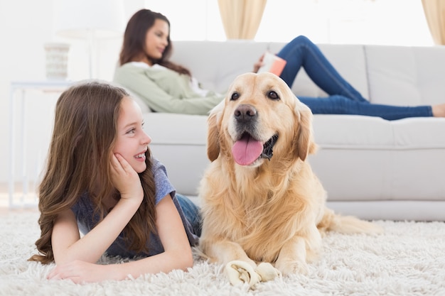 Girl looking at dog while lying on rug