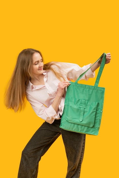 Photo girl looking at the shopper bag young woman holding fashionable textile green bag studio portrait isolated on yellow background