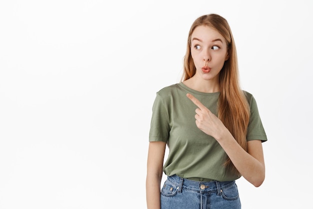 Girl looks interested and excited at left side promo offer pointing and staring aside at special deal banner showing advertisement standing over white background