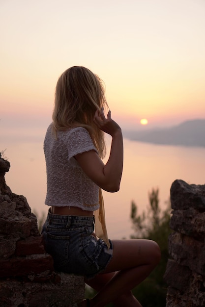 The girl looks at the sea sunset from a high point. Vertical photo with woman back