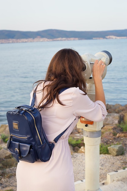 The girl looks through the telescope at the sea