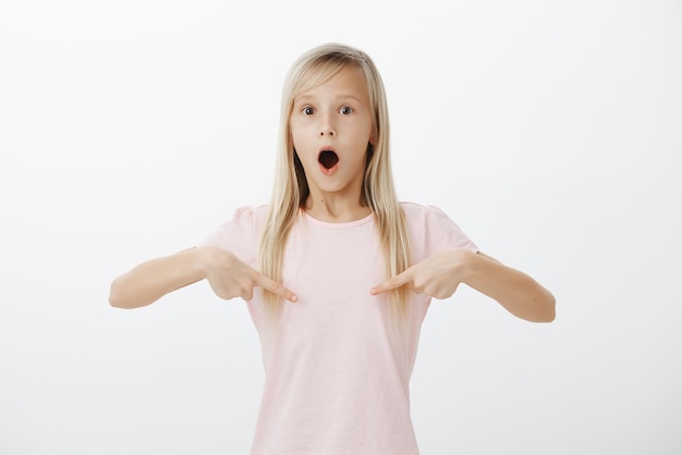 Girl loosing speech from amazement. Portrait of surprised shocked cute daughter with fair hair, pointing at chest with index fingers