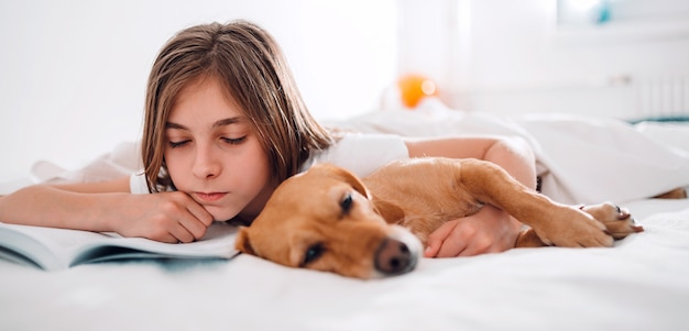 Girl lying in the bed with her dog and reading book