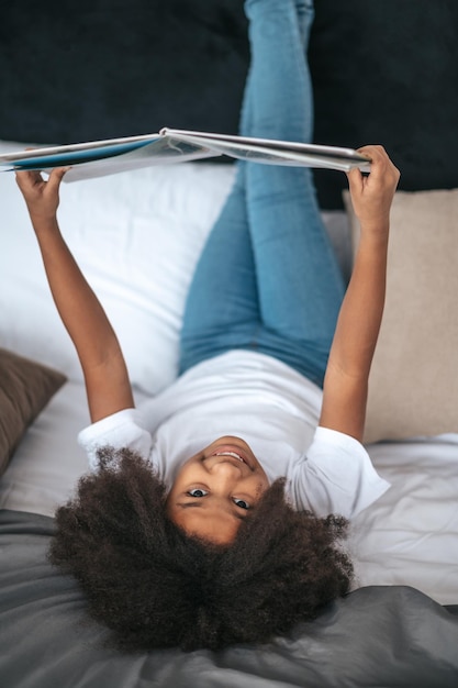 A girl lying on bed with her legs up and reading a magazine