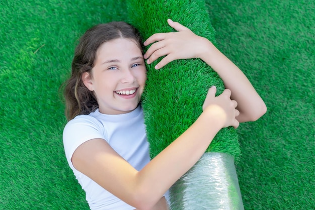 Girl lying on the lawn and hugging a new roll of artificial turf Soft and squishy grass ready to lay