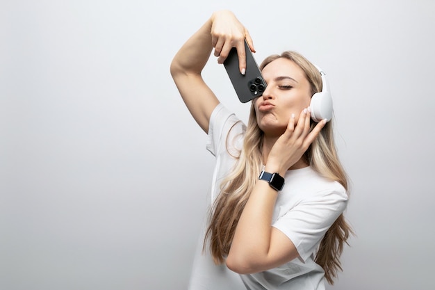 Girl makes a face in wireless headphones with a smartphone in her hands on a white background