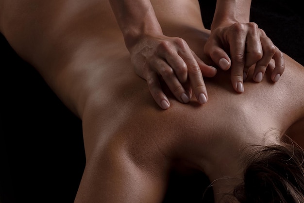 A girl makes a massage with oil closeup on a dark background