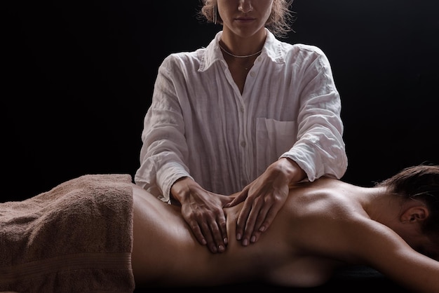 A girl makes a massage with oil closeup on a dark background