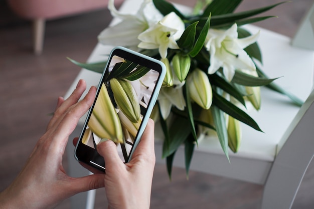 The girl makes a photo on the phone. Photographs a bouquet of white lilies. Mobile photography training. No visible logos.