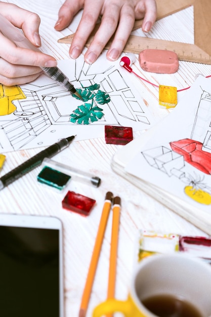 Girl  makes a sketch of the interior. the hand of the girl artist and  sketch, markers, pencil, eraser, ruler, paints, calculator on a wooden background